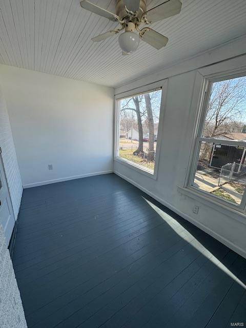 empty room featuring a healthy amount of sunlight, a ceiling fan, dark wood-type flooring, and baseboards