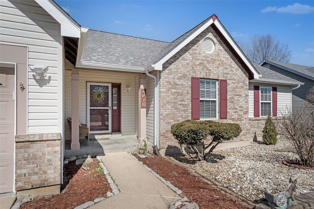 doorway to property with an attached garage, brick siding, and roof with shingles