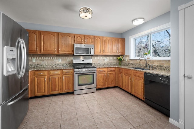 kitchen featuring light stone counters, stainless steel appliances, brown cabinetry, and a sink