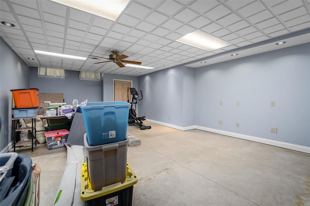 interior space featuring a paneled ceiling, baseboards, concrete flooring, and a ceiling fan