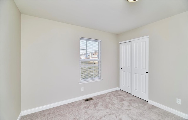 unfurnished bedroom featuring a closet, visible vents, light colored carpet, and baseboards