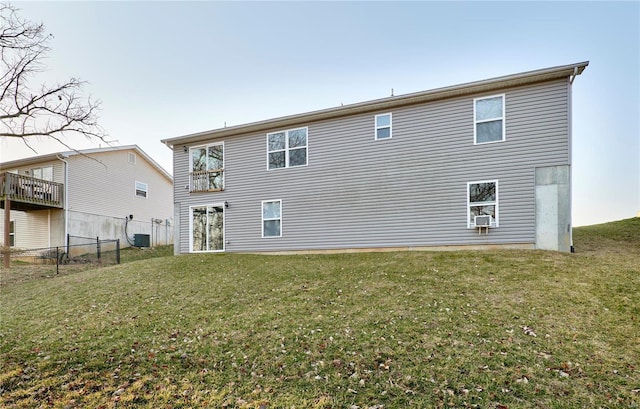 rear view of house with central AC unit, cooling unit, a lawn, and fence