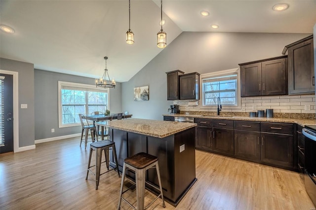 kitchen featuring a kitchen island, a breakfast bar, a sink, dark brown cabinets, and a wealth of natural light