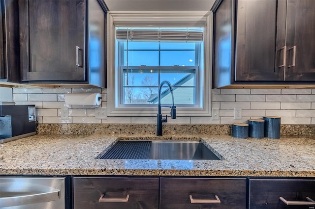 kitchen featuring a sink, tasteful backsplash, dark brown cabinetry, and light stone countertops