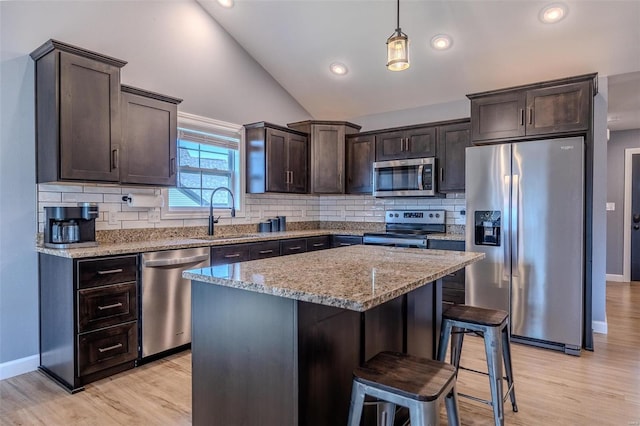 kitchen featuring a sink, stainless steel appliances, dark brown cabinetry, lofted ceiling, and light stone countertops