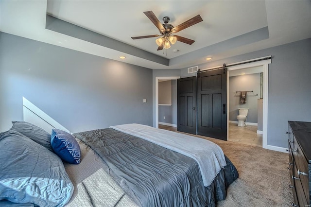 bedroom with visible vents, a tray ceiling, a barn door, baseboards, and light colored carpet