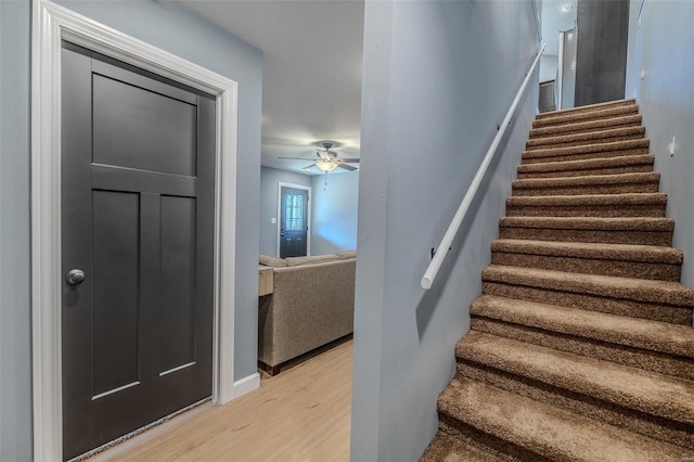 staircase with a ceiling fan and wood finished floors