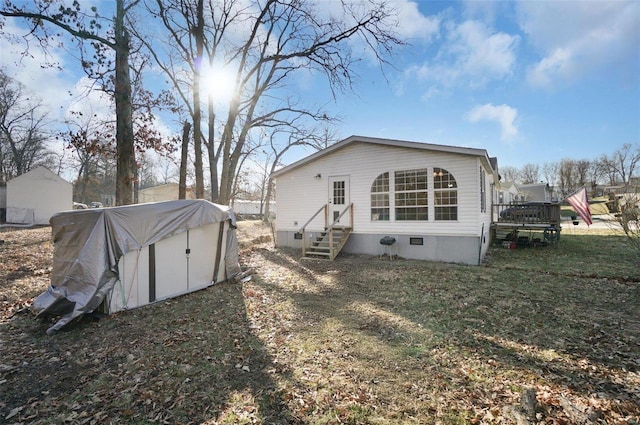 rear view of property with crawl space, entry steps, a storage unit, and an outbuilding