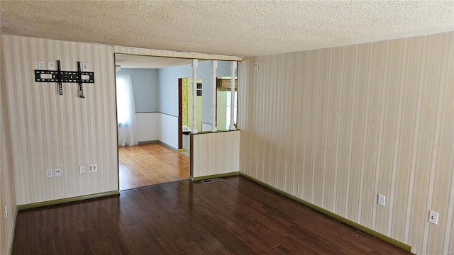 spare room with visible vents, a textured ceiling, wallpapered walls, baseboards, and dark wood-style flooring