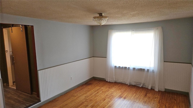 spare room with a wainscoted wall, a textured ceiling, and wood finished floors