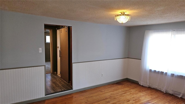 unfurnished room with a wainscoted wall, a healthy amount of sunlight, a textured ceiling, and wood finished floors