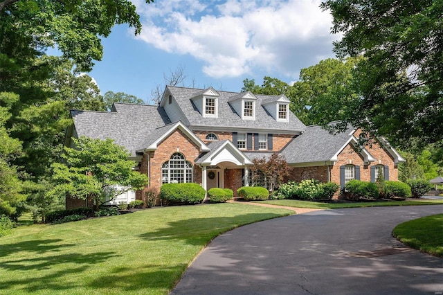 view of front of house with brick siding, curved driveway, a shingled roof, and a front lawn