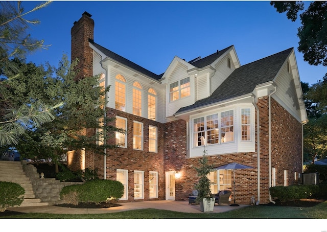 view of front of property with stairway, a patio area, brick siding, and a chimney