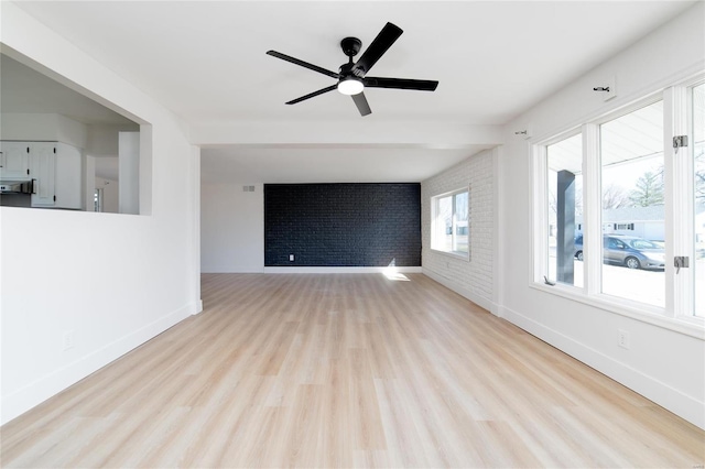 unfurnished living room featuring brick wall, a ceiling fan, baseboards, and wood finished floors