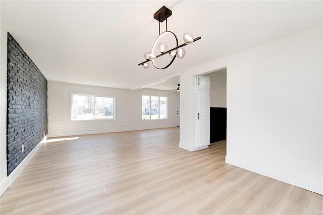 empty room with light wood-style flooring, baseboards, brick wall, and ceiling fan with notable chandelier