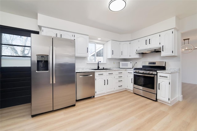 kitchen featuring light wood finished floors, a sink, under cabinet range hood, appliances with stainless steel finishes, and white cabinetry