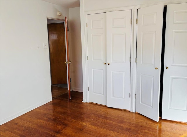 unfurnished bedroom with wood finished floors, multiple closets, and baseboards