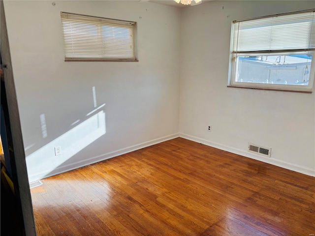 empty room with visible vents, wood-type flooring, and baseboards