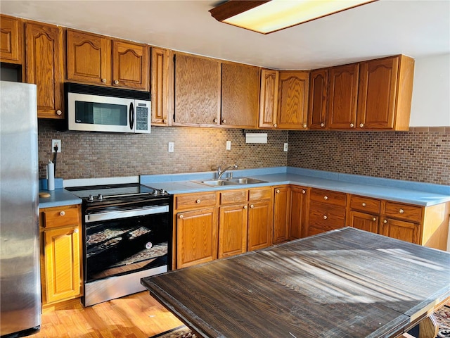 kitchen featuring brown cabinetry, light wood finished floors, a sink, stainless steel appliances, and tasteful backsplash