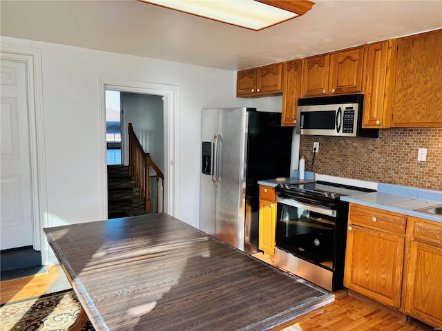 kitchen featuring light countertops, decorative backsplash, light wood-style flooring, brown cabinetry, and stainless steel appliances