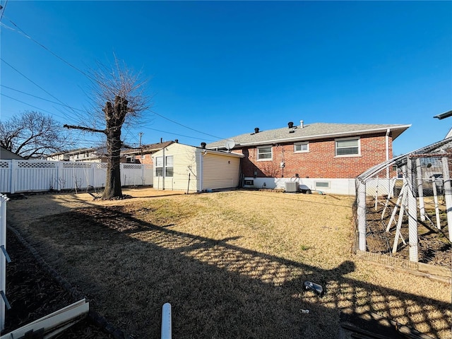 rear view of property featuring a lawn, fence, an outdoor structure, brick siding, and central AC unit