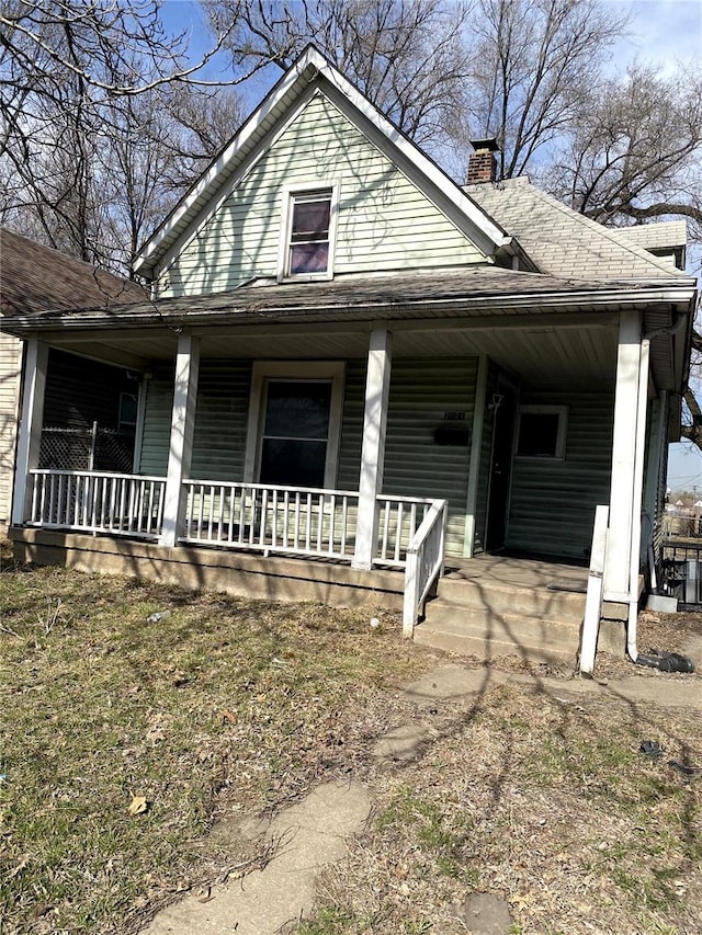 view of front of home featuring a porch, a chimney, and a shingled roof