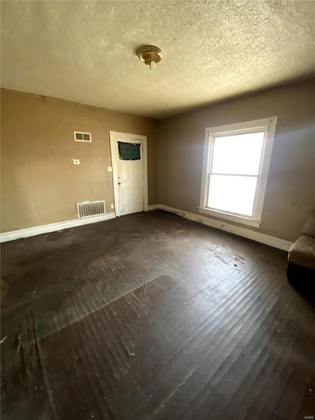 unfurnished living room with visible vents, baseboards, a textured ceiling, and wood finished floors