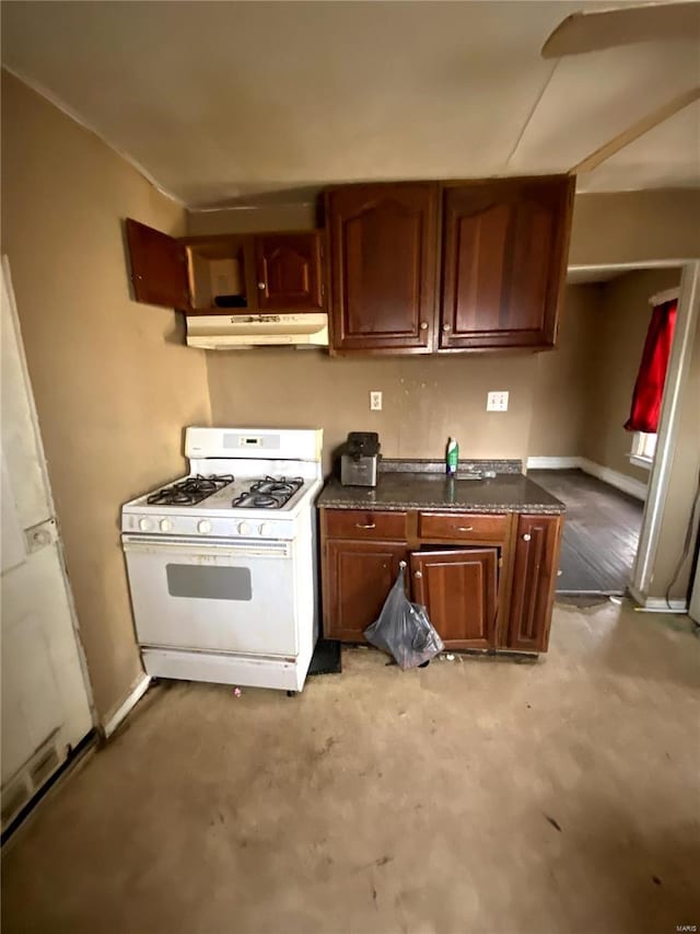 kitchen featuring dark countertops, concrete floors, baseboards, gas range gas stove, and under cabinet range hood