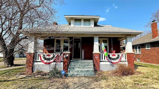 bungalow-style home featuring a porch, a front yard, and roof with shingles