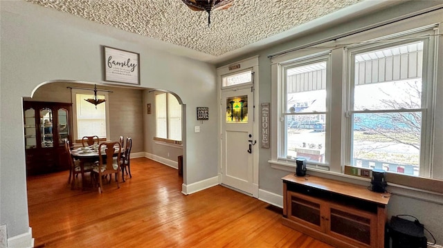 entrance foyer featuring baseboards, arched walkways, a healthy amount of sunlight, and light wood-style flooring