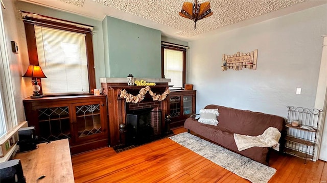 living room featuring a wealth of natural light, a brick fireplace, a textured ceiling, and hardwood / wood-style flooring