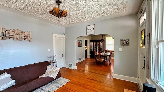 living room featuring wood finished floors, arched walkways, a wealth of natural light, and baseboards