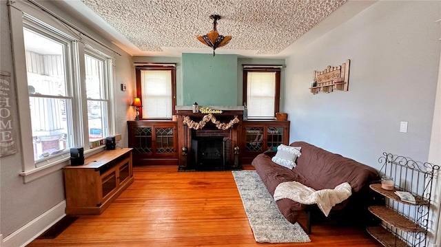 living room with light wood-style flooring, a fireplace, baseboards, and a textured ceiling