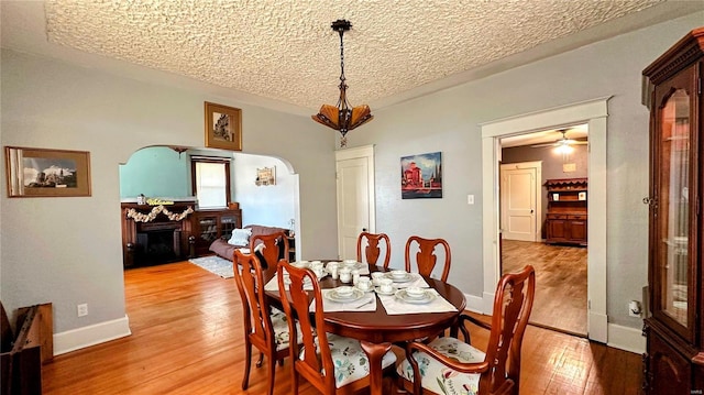 dining area with baseboards, a fireplace, arched walkways, a textured ceiling, and light wood-type flooring