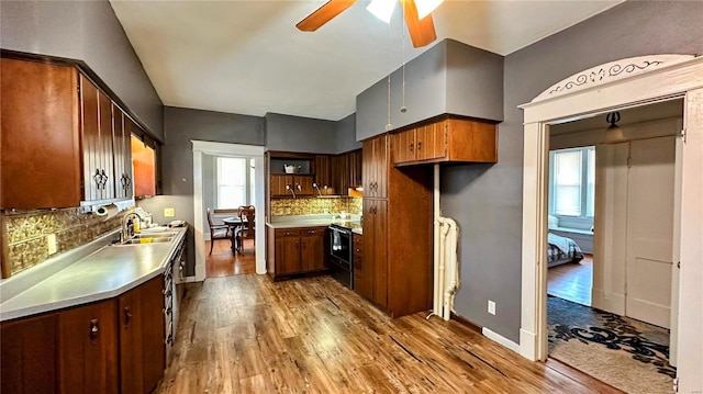 kitchen featuring a ceiling fan, stainless steel countertops, backsplash, radiator heating unit, and dark wood-style flooring