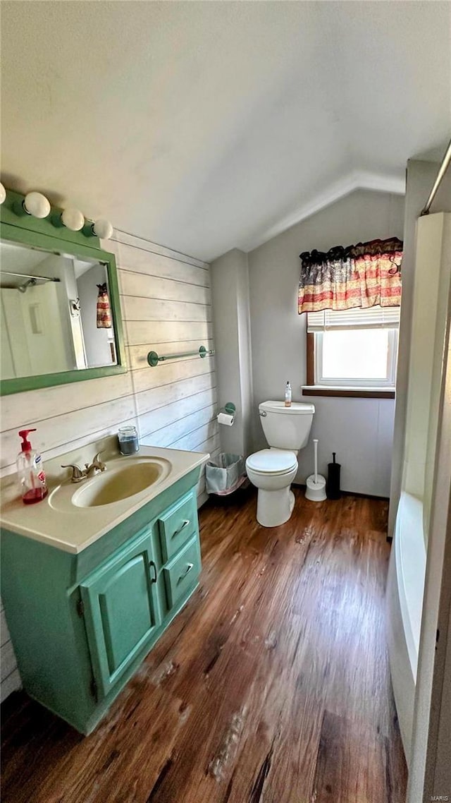 bathroom with toilet, wood finished floors, walk in shower, vanity, and vaulted ceiling