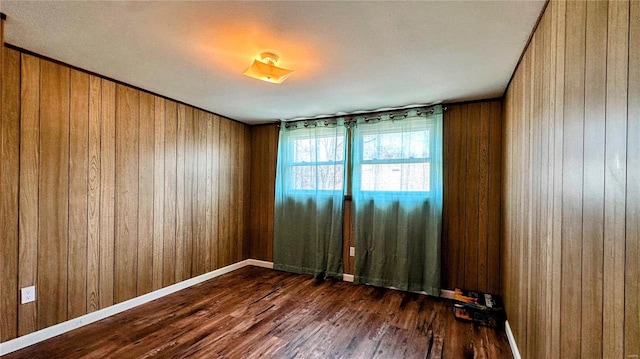 spare room featuring baseboards, dark wood-type flooring, and wooden walls