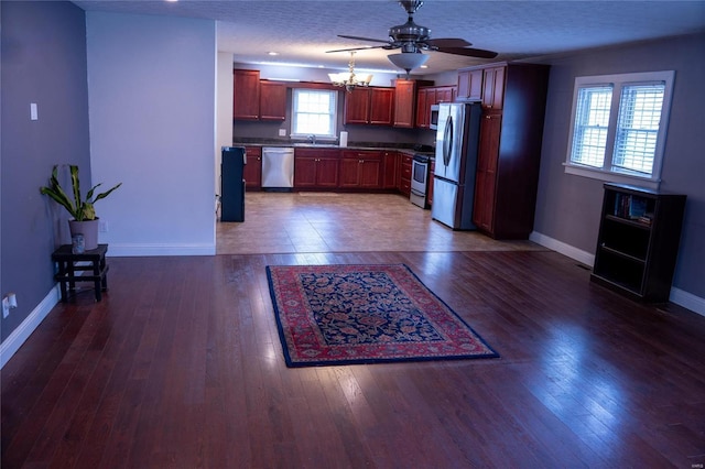 kitchen with dark wood-type flooring, baseboards, ceiling fan with notable chandelier, appliances with stainless steel finishes, and a textured ceiling