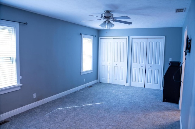 unfurnished bedroom with carpet, visible vents, baseboards, ceiling fan, and multiple closets