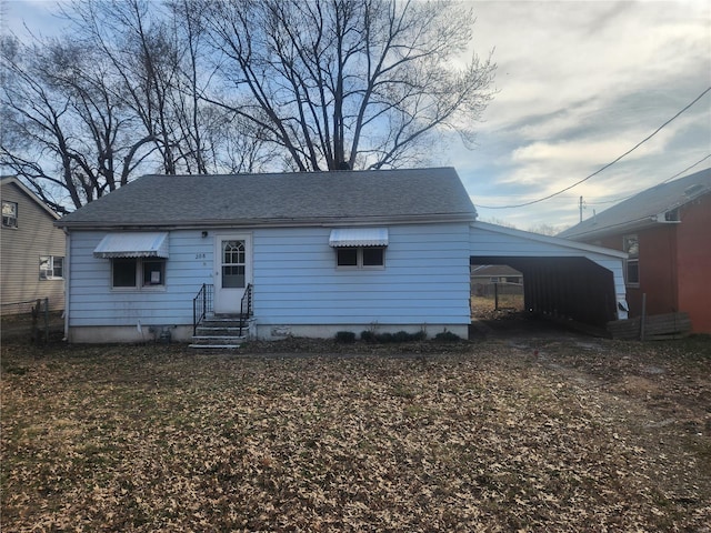 back of house with entry steps, an attached carport, and a shingled roof