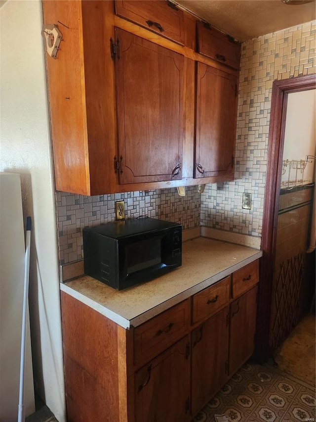 kitchen featuring brown cabinetry, backsplash, light countertops, and black microwave