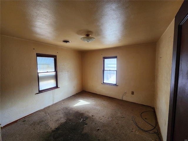 unfurnished room featuring visible vents and a textured wall