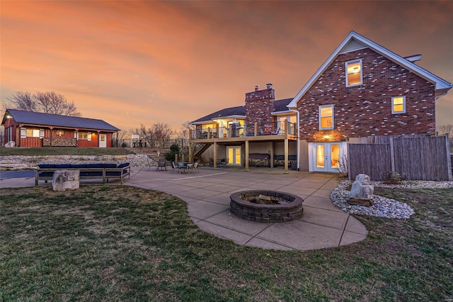 back of house at dusk featuring brick siding, a fire pit, a lawn, a deck, and a patio area