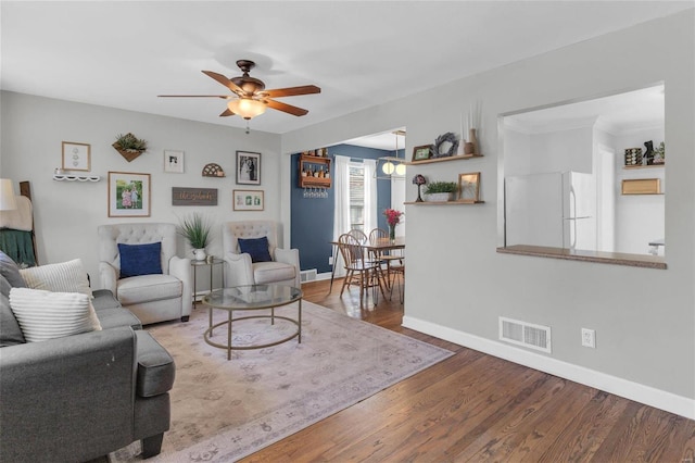 living room featuring a ceiling fan, wood finished floors, visible vents, and baseboards