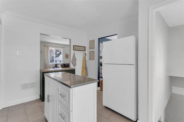 kitchen featuring visible vents, white cabinetry, freestanding refrigerator, light tile patterned flooring, and crown molding