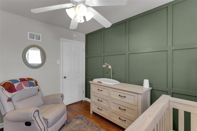 bedroom with dark wood-type flooring, a decorative wall, visible vents, and ceiling fan