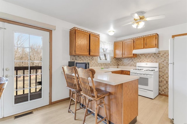 kitchen featuring visible vents, light wood-type flooring, under cabinet range hood, white appliances, and light countertops