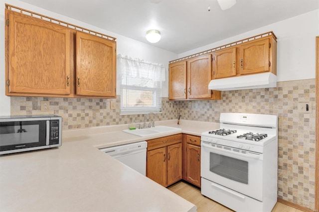 kitchen with under cabinet range hood, a sink, white appliances, light countertops, and decorative backsplash