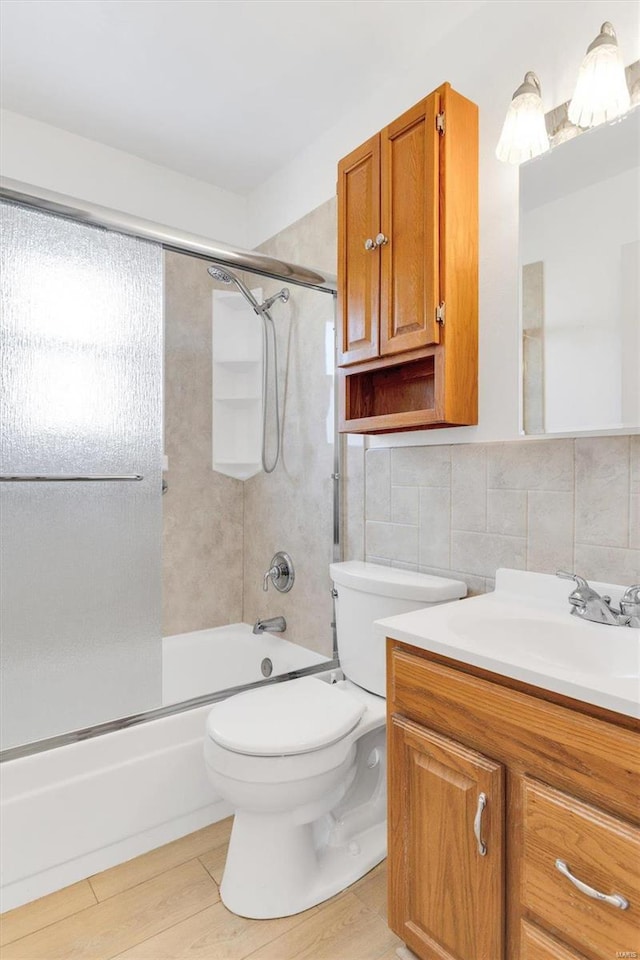 bathroom with toilet, wood finished floors, tile walls, enclosed tub / shower combo, and vanity