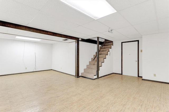 finished basement with a drop ceiling, baseboards, light floors, and stairway